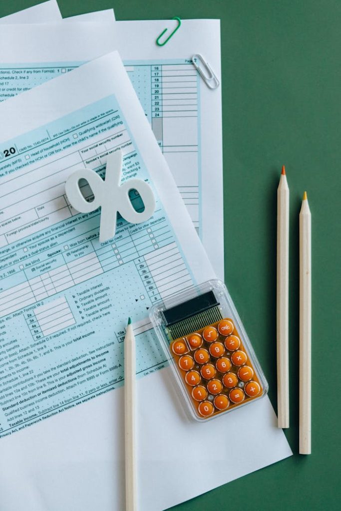 Flat lay of tax documents, calculator, and pencils on green surface.